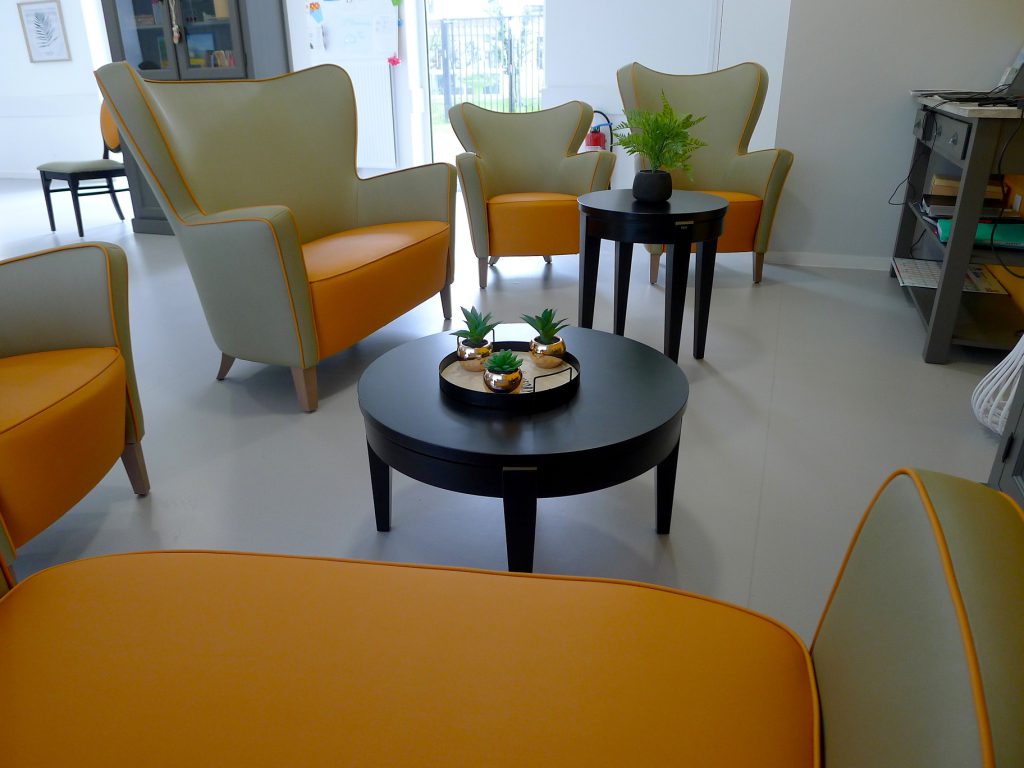 Salon du PASA, fauteuils orange, tables basses noires, plantes, 